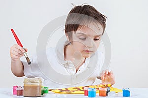 Boy looks closely at the paints and drawing. He thinks he will still paint