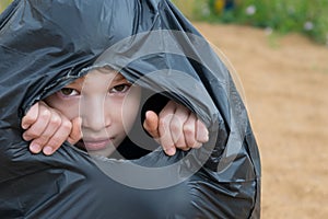 Boy looks through the hole of a black garbage bag, close-up