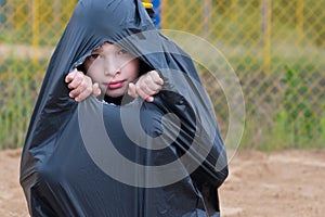 The boy looks through the hole of a large black garbage bag, single children