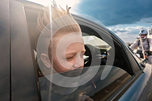 The boy looks out of the car window. The child's hair is blown by the wind