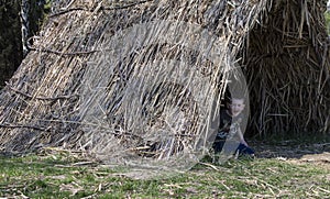 The boy looks out of the straw tent.