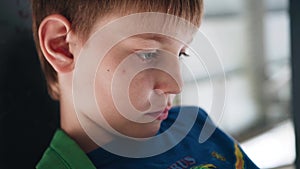 The boy looks thoughtfully at the screen of the smartphone. The boy sits under the bridge. Close up. Emotions.