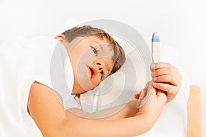 Boy lying in bed and checking thermometer readings