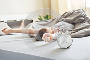 Boy lying on bed near alarm clock in the morning, stretching and yawns