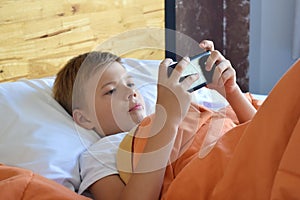 Boy lying in bed with a telephone. Mobile children`s dependence.