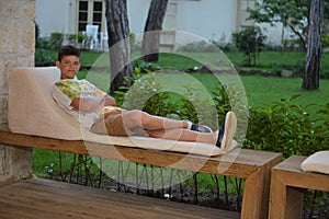 Boy lying on the bench outdoors in the evening. Portrait of teen boy with dark hair. Charming young male in fashionable