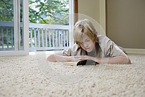 Boy 10-12 lying on carpet reading book