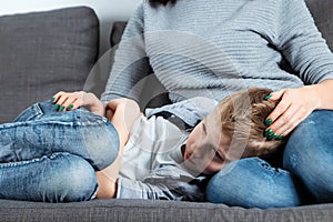 The boy is lying on the couch with an abdominal pain near his mother. The concept of custody, parental care, stomach problems,