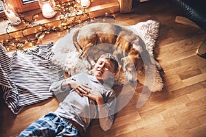 Boy lying on the floor and near beagle dog sleeping on sheepskin in cozy home atmosphere