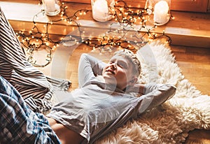 Boy lying on the floor and smiling on sheepskin in cozy home atmosphere and dreaming about Christmas presents. Peaceful moments of