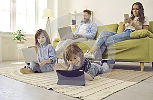 Boy lying on floor with tablet while mom, dad and brother are using their own devices