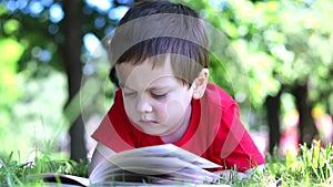 The boy is lying on the grass and reading a book . Extracurricular reading. Offline training.