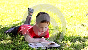 The boy is lying on the grass and reading a book . Extracurricular reading. Offline training.