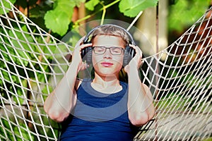 Boy lying in a hammock and listen to music on headphones. Summer