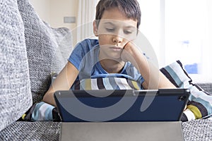 Boy lying on sofa with digital tablet computer at home. Technology, ditance education, online learning, playing games