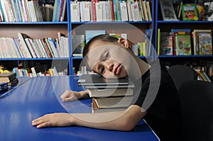 Boy lying tired on pile of book in library don`t want to learning