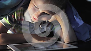 Boy lying under blanket and watching cartoon on touch pad