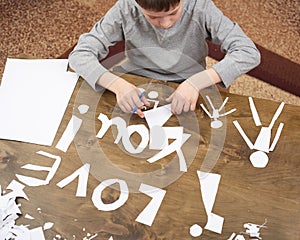 Boy makes origami - car and family, children, parent, I love you text, top view on wood background