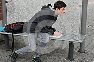 Boy makes school homework at the bus stop