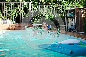 Boy making big splash on inflatable crocodile whilst swimming in backyard pool