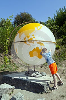 The boy is making an effort to rotate the earth in the form of a globe