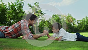 Boy and man armwrestling on grass. Father and son practising arm wrestling