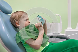 Boy man child at dentist in chair look at white teeth. Curious, serious look. Oral health and hygiene concept