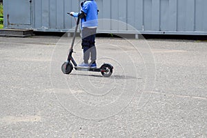 A boy, a man rides along the park road on a new modern electric scooter on batteries, standing on it with two legs