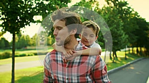 Boy and man walking on street. Portrait of joyful father carrying son on back