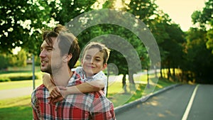 Boy and man walking on street. Portrait of joyful father carrying son on back