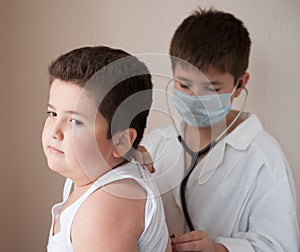 Boy in the mask and costume of the doctor listens to the heart rate of fat boy