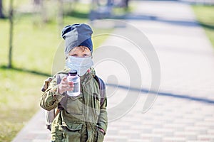 A boy in mask holds a bottle of water in hand