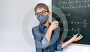 Boy with mask solving math exercises on blackboard