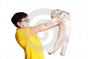 A boy in a medical mask holds his white cat at arms length