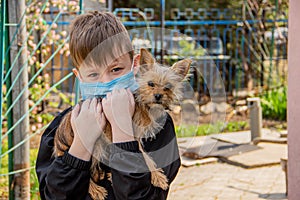 A boy in a medical mask with a small dog walks on the street during a flu coronavirus pandemic, air pollution