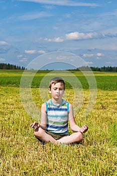 Boy meditating on the green field