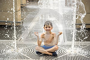 Boy meditating in water fountain find ZEN. Child playing with a city fountain on hot summer day. Happy kids having fun in fountain