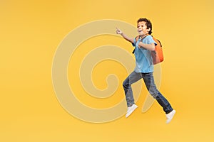 Boy in mid-stride pointing excitedly, yellow backpack