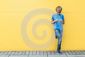 Boy with mobile cell phone standing near yellow wall outdoors