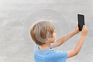 Boy with mobile phone. Child taking photo with his smartphone. Gray urban background. Back view. Technology concept