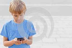 Boy with mobile phone in the street. Child looking at the screen, playing games, using apps. City background. School