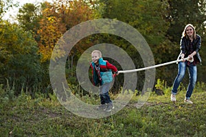 Boy and mom pulling the rope in nature in the autumn forest