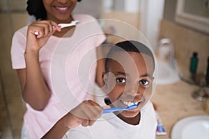 Boy with mother brushing teeth at home