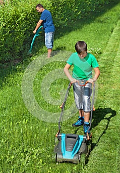 Boy mowing the lawn with man trimming at the edges