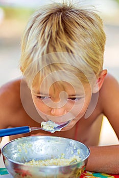 A boy in nature eats porridge.