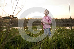 Boy in nature standing in a lake with the sunset behind him.