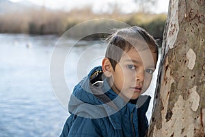 A boy near the tree by the river with expressionless gaze