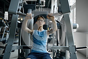 Boy nerd exercising using professional sports gym equipment