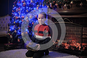 The boy next to a glowing blue Christmas tree and fireplace