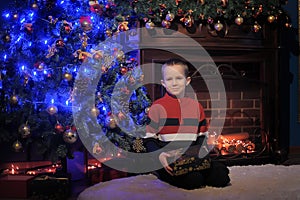 The boy next to a glowing blue Christmas tree and fireplace
